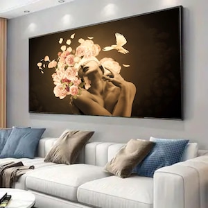May include: A large framed canvas art print depicts a woman with a floral headpiece and a dove. The artwork features a sepia tone with pink and white flowers. The woman's eyes are covered, and she is reaching up with her hand.