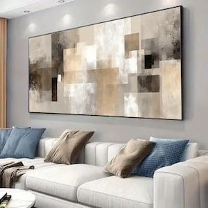 Peut inclure: Tableau abstrait avec un design géométrique aux tons neutres. L'œuvre d'art est composée de rectangles et de carrés superposés dans des tons beige, marron et gris, encadrés en noir. Le tableau est accroché au-dessus d'un canapé blanc avec des coussins bleus et marron.
