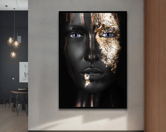 May include: A black and gold portrait of a person with blue eyes. The person's face is painted with gold leaf on one side and black paint on the other side.