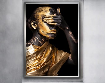 May include: A woman with black and gold paint on her face and body, covering her eyes with her hand. She is wearing a gold fabric draped around her shoulders.