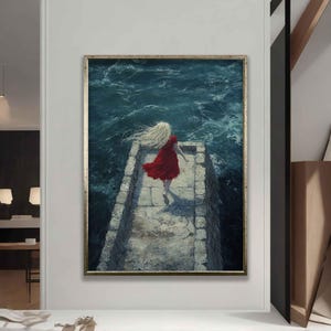 May include: A framed art print depicting a woman in a red dress running along a stone pier towards a stormy sea. The artwork is set in a gold frame and hung on a white wall. The woman has long, blonde hair blowing in the wind.