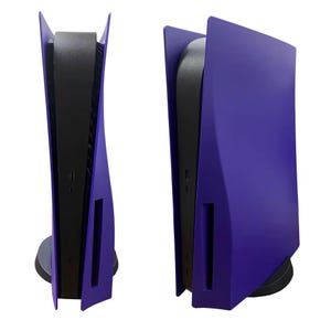 May include: Two purple game consoles are displayed side-by-side against a white background. The consoles have a sleek, modern design with a black center and purple side panels. The consoles are standing upright on a black base.