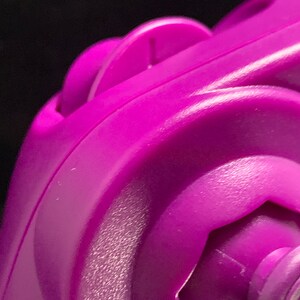 May include: Close-up of a vibrant purple plastic object with curved edges and a textured surface. The object features a circular design with a central, hexagonal element and a smaller, circular part.