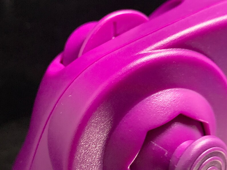 May include: Close-up of a vibrant purple plastic object with curved edges and a textured surface. The object features a circular design with a central, hexagonal element and a smaller, circular part.