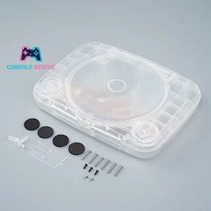 May include: A transparent PlayStation 1 console shell kit, featuring screws, buttons, and rubber feet. The Console Revive logo is visible. The clear shell allows for a view of the console's internal components. Ideal for customisation or replacement.