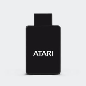 May include: A black Atari game cartridge with the Atari logo in white. The cartridge has a rectangular body with a smaller, rectangular connector at the top. The background is a solid, light grey.
