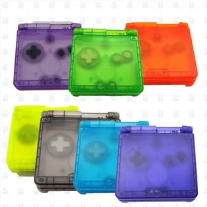 Può includere: Una collezione di console Game Boy Advance SP traslucide e colorate. Le console sono in vari colori, tra cui viola, verde, arancione, giallo, grigio, blu e un'altra tonalità di viola. Ogni console ha pulsanti visibili e uno schermo.