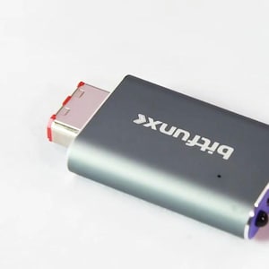 May include: A gray Bitfunx USB adapter with a purple accent on the end. The adapter has a USB-C connector with red accents. The text "Bitfunx" is printed on the device. The Console Revive logo is in the upper left corner.