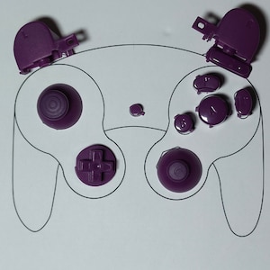 May include: A collection of purple video game controller components, such as buttons and analogue sticks, are laid out on a white surface with a controller outline. The parts are of different shapes and sizes, indicating a disassembly or repair task.