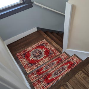 Puede incluir: Alfombras y alfombrillas a juego con diseños rojos y azules sobre escaleras de madera oscura. La alfombra y las alfombrillas tienen un aspecto envejecido y vintage. Las alfombrillas son rectangulares y se ajustan al ancho de los escalones.