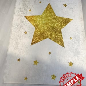 May include: A white rug with a large gold glitter star in the center. The rug is decorated with smaller gold glitter stars.