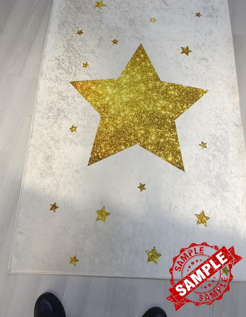 May include: A white rug with a large gold glitter star in the center. The rug is decorated with smaller gold glitter stars.
