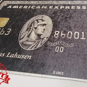 以下が含まれることがあります： 金色のエンボス加工されたロゴと白い文字で「AMERICAN EXPRESS」と書かれた黒いアメリカン・エキスプレスのクレジットカード。カード番号は3763 86001で、ロゴの下に「Dr. Nikolaus Lahusen」という名前が印刷されています。カードには「MEMBER SINCE 00」と「AMEX」の文字も印刷されています。