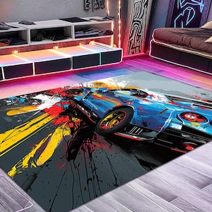 May include: A rectangular area rug featuring a vibrant, abstract graphic print of a blue sports car. The design incorporates bold splashes of yellow, red, and black paint-like textures across the surface, creating a dynamic, high-contrast visual effect.
