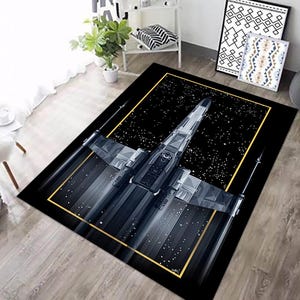 Könnte beinhalten: Schwarzer rechteckiger Teppich mit einer detaillierten Illustration eines Raumjägers in Grau- und Silbertönen vor einem sternenklaren schwarzen Hintergrund. Der Teppich hat einen goldenen Rand.