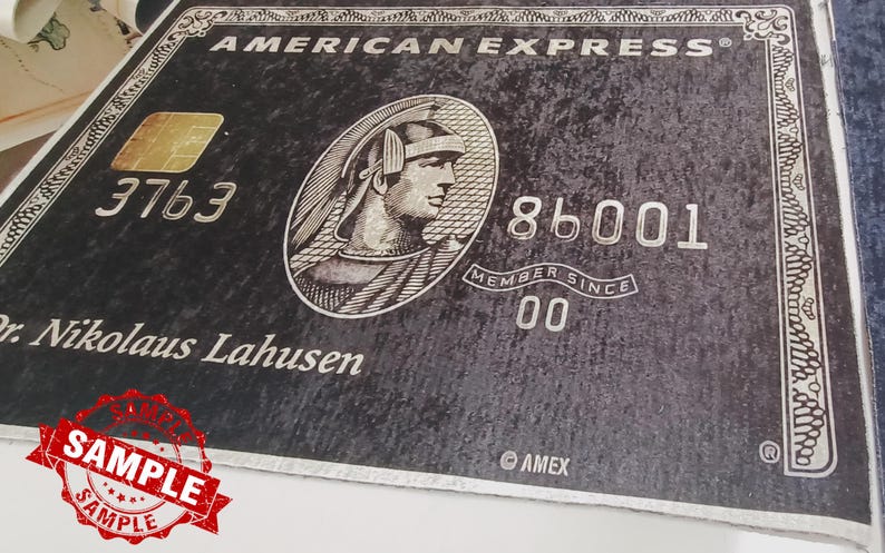 May include: A black American Express credit card with a gold embossed logo and the text "AMERICAN EXPRESS" in white. The card number is 3763 86001 and the name "Dr. Nikolaus Lahusen" is printed below the logo. The card has a silver border and the text "MEMBER SINCE 00" is printed below the card number.