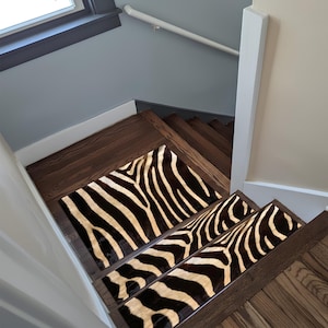 Puede incluir: Escalera de madera con peldaños con estampado de cebra. Los peldaños tienen un patrón negro y crema, creando un contraste con los escalones de madera oscura. Las paredes están pintadas en tonos neutros.