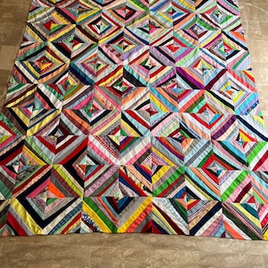 Könnte beinhalten: Ein farbenfroher Quilt aus Stoffstreifen, die in einem Diamantenmuster zusammengenäht sind. Der Quilt besteht aus vielen verschiedenen Farben, darunter Rot, Blau, Grün, Gelb und Pink.