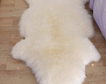 May include: A white sheepskin rug with a soft, fluffy texture. The rug is laid out on a wooden floor.