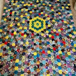 May include: A large quilt made of colorful fabric scraps sewn together in a hexagonal pattern. The quilt is yellow, blue, green, red, and purple. The center of the quilt has a large yellow hexagon with a green and yellow pattern.