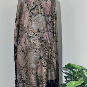 May include: A floral patterned shawl with a black fringe. The shawl features a design of pink and gold flowers on a black background. The shawl is draped over a form.