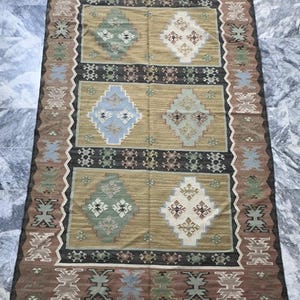 May include: A brown, beige, blue, and green patterned rug with a geometric design. The rug has a fringe border.