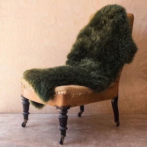May include: A dark green sheepskin throw draped over a vintage armchair with wooden legs and wheels. The chair is upholstered in a beige fabric with visible stitching.