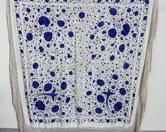 May include: A white shawl with detailed blue floral embroidery and bird motifs. The shawl has a fringed trim and a decorative border. The design includes roses and other floral elements.