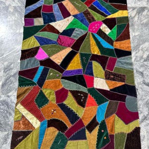 Könnte beinhalten: Eine bunte Patchwork-Decke aus Samtstoff in verschiedenen Grüntönen, Blau, Rot, Lila und Braun. Die Decke ist mit einem dekorativen Steppstich zusammengenäht.
