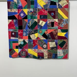 Puede incluir: Una colcha de retazos colorida hecha de varias telas en tonos de rojo, azul, verde, amarillo y marrón. La colcha está hecha de cuadrados y triángulos, y la tela es una mezcla de patrones y texturas.