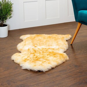 May include: A soft, fluffy, golden yellow faux fur rug with a white undercoat. The rug is laid out on a wooden floor.