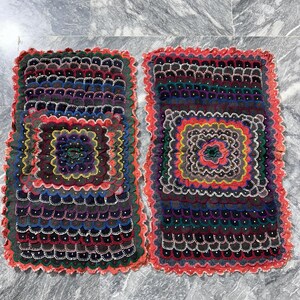 May include: Two handmade square embroidered throw pillows with colorful floral patterns and scalloped edges. The pillows are made of a dark fabric with a red border and are decorated with colorful embroidery.