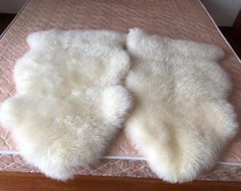 May include: Two off-white sheepskin rugs with a soft, fluffy texture. The rugs are placed side-by-side on a bed, showcasing their natural shape and color. The rugs are ideal for adding warmth and comfort to any room.