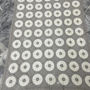 May include: A large, crocheted tablecloth with a repeating pattern of white circles on a gray background.