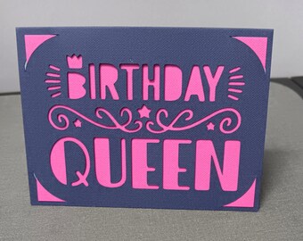 May include: A navy blue card with a pink "Birthday Queen" design. The card has a crown and swirls around the text.