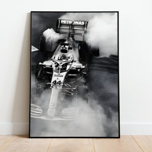 May include: A black and white photograph of a race car speeding through a cloud of smoke. The car is a Formula 1 car with the number 44 on the side and the word "PETRONAS" on the rear wing.