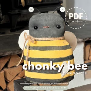 May include: A handmade stuffed bee with a grey head, black eyes, and a yellow and black striped body. The bee has white wings, a jute twine accent, and the text "chonky bee pattern & tutorial". The image also includes the text "PDF download".