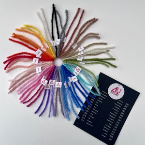 Könnte beinhalten: Eine Farbkarte mit Garnproben, die in einem Kreis angeordnet sind. Die Garnfarben reichen von Weiß bis Schwarz, mit Schattierungen von Rot, Orange, Gelb, Grün, Blau, Lila und Rosa. Die Garnproben sind mit Nummern gekennzeichnet.