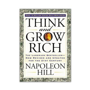 May include: A book cover for "Think and Grow Rich" by Napoleon Hill. The title is in large black letters with a gold-colored graphic. The cover is framed by a border of money.