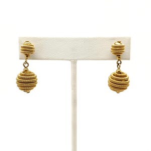 May include: A pair of gold-toned drop earrings with a coiled wire design. The earrings feature two round balls, one smaller and one larger, connected by a chain.