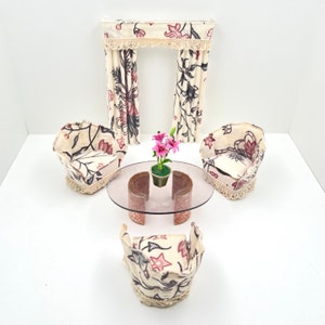 Puede incluir: Un conjunto de sala de estar en miniatura con un sofá estampado floral, dos sillones, una mesa de café de vidrio y un valance de cortina estampado floral.