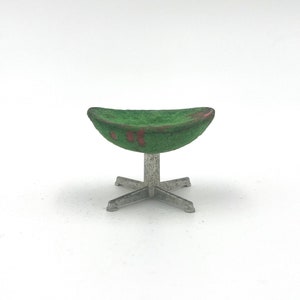 Op de afbeelding: Een kleine groen en rood gestoffeerde stoel met een zilverkleurige metalen basis. De stoel heeft een gebogen zitting en een vierpotige basis. Het is waarschijnlijk een poppenhuis- of miniatuurmeubelstuk.