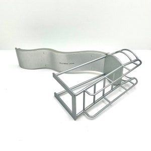 Può includere: Organizzatore da bagno in metallo argentato con un ripiano curvo e una griglia in filo metallico con un design a scala.