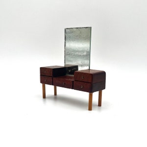 May include: A wooden vanity set with a mirror and four drawers. The vanity is made of dark wood with light wood legs. The mirror is rectangular and has a silver frame.