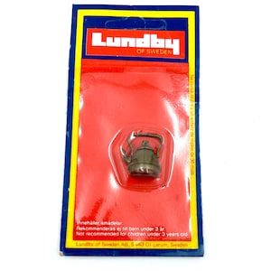 May include: A small, brown metal teapot on a red and white packaging card. The card reads "Lundby of Sweden" and includes a warning that the product is not recommended for children under 3 years old.