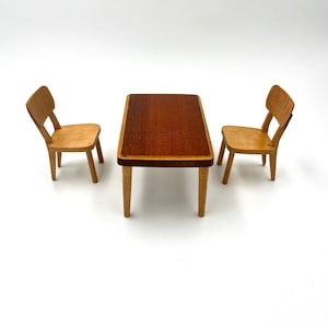 May include: A miniature wooden dining set comprising a rectangular table with a dark brown top and two matching chairs. The table is about 10 cm long. The chairs have a classic design.