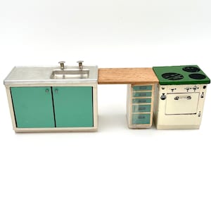 May include: A miniature kitchen set featuring a sink with teal cabinets, a wooden countertop, a cabinet with drawers, and a stove. The stove has a green top with black burners and a white oven door. The set is made of wood and metal.