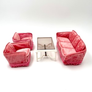 May include: A pink velvet living room set featuring a sofa, two armchairs, and a glass-topped coffee table. The furniture is in a vintage style with a delicate, feminine aesthetic.