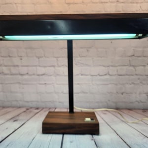 May include: A vintage black and wood desk lamp with a fluorescent light fixture. The lamp has a black metal base and a wooden shade.