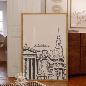 May include: A framed print featuring a black and white illustration of Philadelphia landmarks, including Independence Hall and the Liberty Bell. The word "philadelphia" is written in script. Two other framed prints are visible in the background.